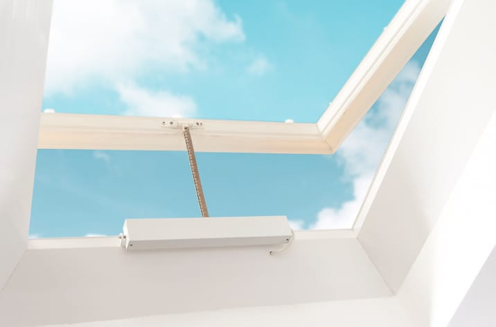 Mingardi Micro Evo1 Actuator fitted to a roof vent. Open skylight with a clear view of the blue sky and white clouds, framed by white walls, enhanced by window actuators for effortless operation.