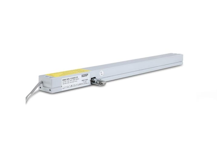A long, rectangular electric actuator with a cable attached. The device, perfect for door automation, is gray and white with labeling and a connector visible on one side.