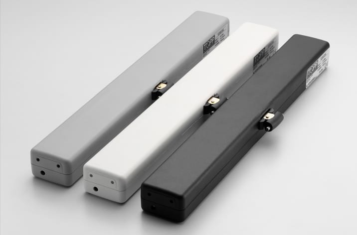 Three elongated rectangular electronic devices in gray, white, and black colors are arranged side by side on a flat surface. Each has a small switch and a label with text, ideal for integration into door automation systems.